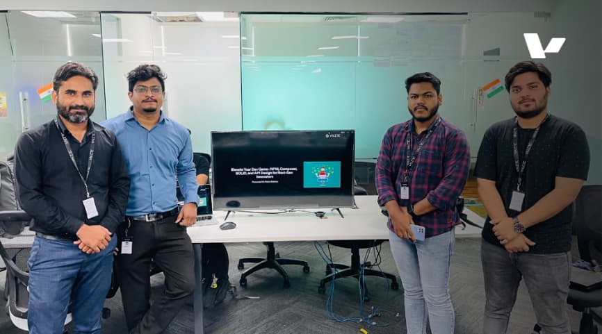 Alt text: Four team members from Valere standing in front of a screen displaying "Elevate Your Dev Game: API Best Practices Workshop" during an internal workshop at the office.