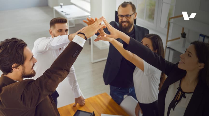 Group of professionals in a modern office celebrating success with a team high-five, symbolizing collaboration, unity, and teamwork.