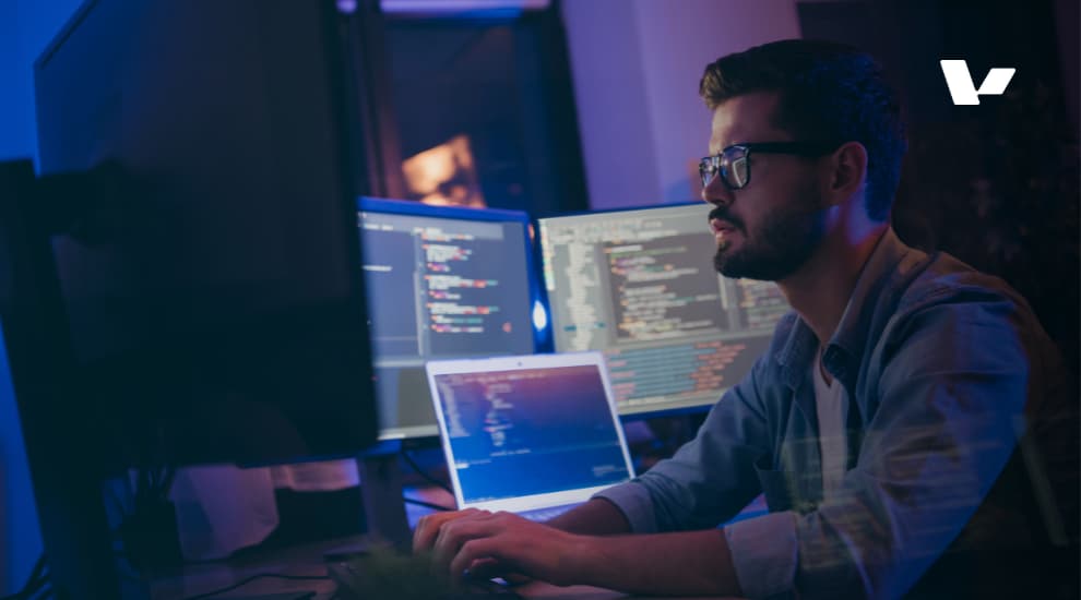A developer focused on coding, working at night with multiple monitors displaying programming code.