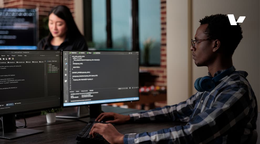 A focused software developer working on machine learning models using dual monitors, with AI-generated code displayed on the screens.
