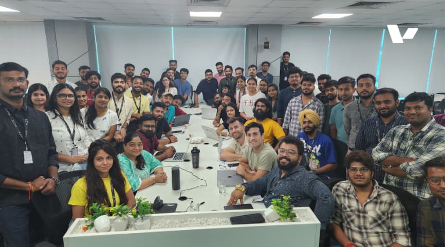 A large group of diverse professionals from the Valere team gathered around a conference table, smiling and posing for a photo in a modern office environment.