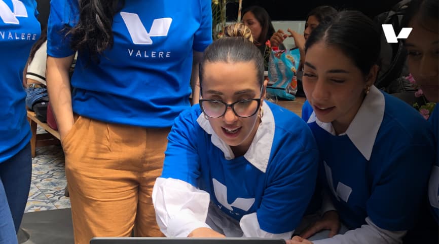 A group of women wearing blue Valere t-shirts collaborating around a laptop, smiling and engaged in a team discussion.