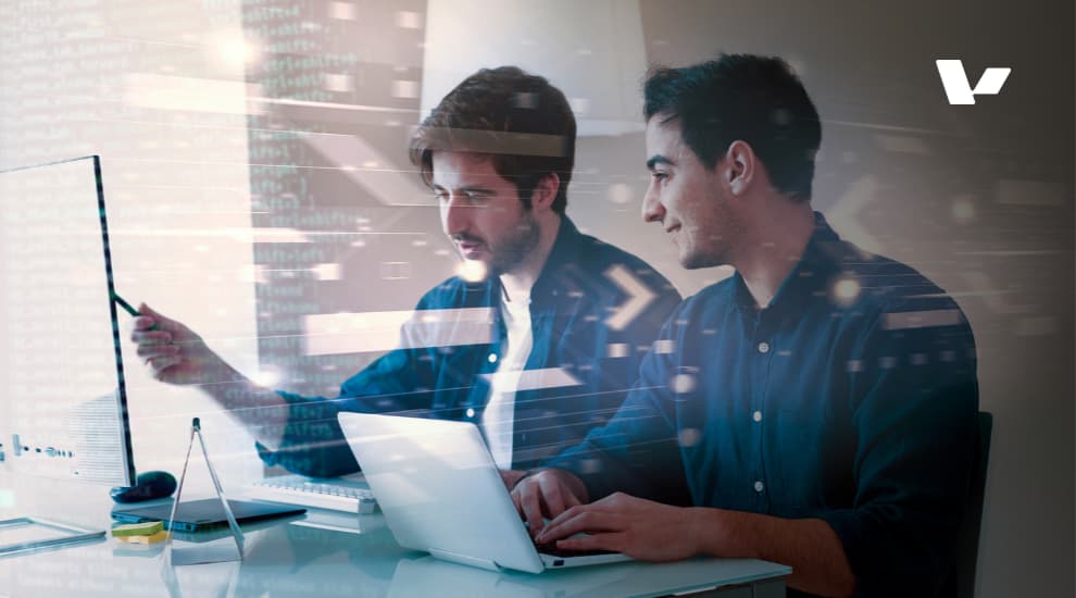 Two software developers collaborating at a desk, discussing code and working on a laptop in a modern office setting, with digital code overlay.