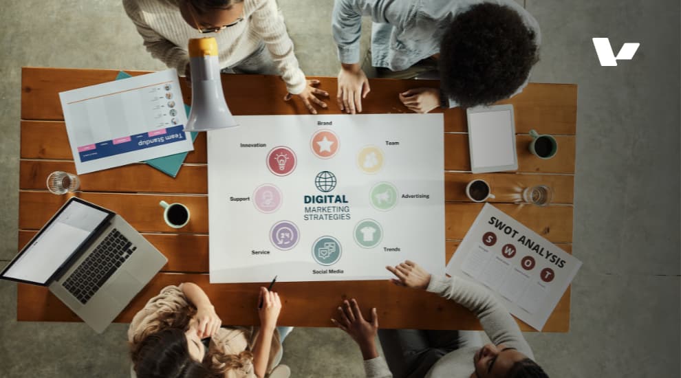 An overhead view of a team collaborating on a digital marketing strategy, with a focus on a chart displaying key areas like brand, innovation, social media, trends, and SWOT analysis.