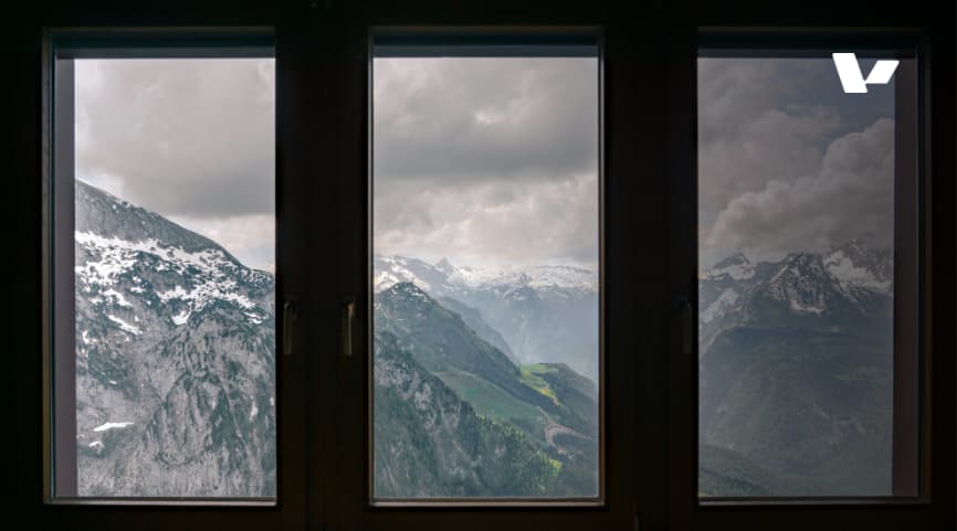 A view of snow-capped mountains through a wooden window with three panes, showcasing the beauty of nature and the vast landscape beyond.